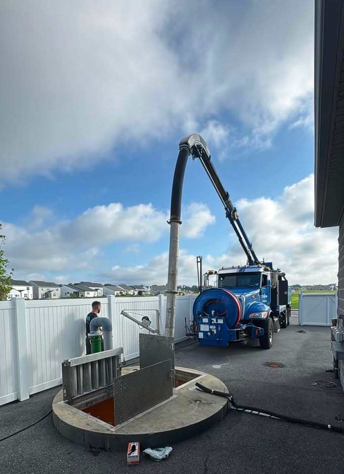 Vacuum hose feeding down into an open wet well beside a residential development